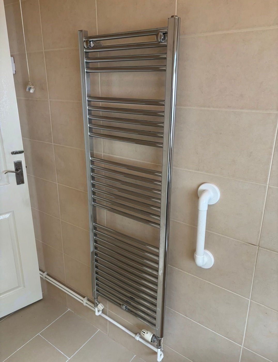 Chrome heated towel rail installed in tiled bathroom